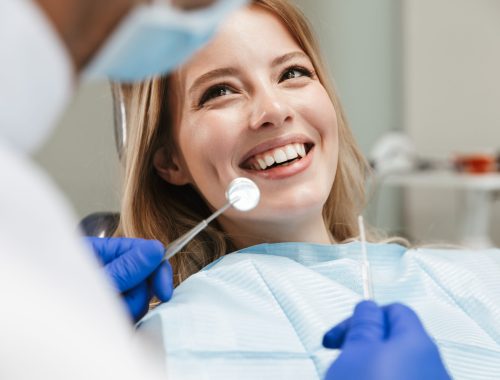 Image of pretty young woman sitting in dental chair at medical center while professional doctor fixing her teeth